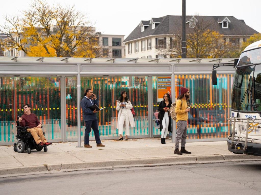 People at a transit shelter waiting for a bus.